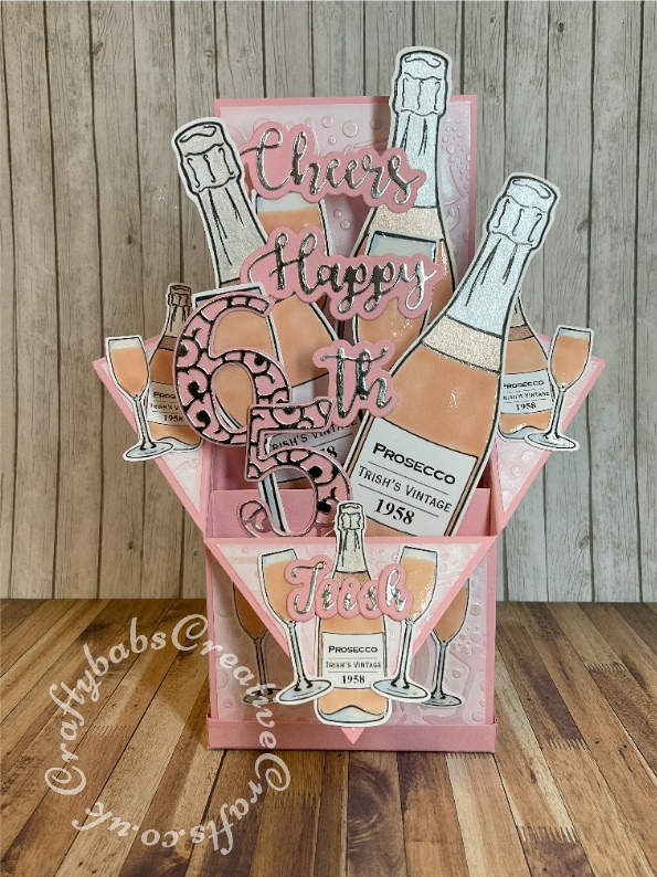 Pink Prosecco themed Pop Up Box card made using various digi-stamps from Craftworld Premium members free digi-stamps cheers collection, dies including; CARD MAKING MAGIC DIE SETS SOLID & OVERLAY NUMBER & SUFFIX, i Craft Cheers & Happy dies, embossing folder and stamps from Issue 161 of Simply cards & Papercraft magazine and Gemini Expressions Uppercase and lower case Alphabet die Sets. -craftybabscreativecrafts.co.uk